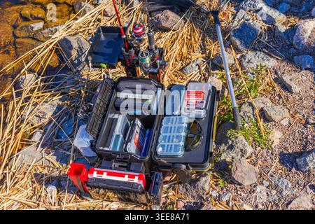 Close up view of Meiho fishing tackle box with rod holders and angling equipment on rocky lakeside shore outdoors. Sweden. Stock Photo