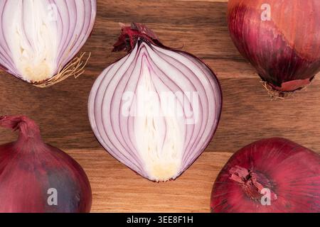Sliced red onion halves on a walnut chopping board. Red  onions are mild & sweet alliums prized for their color and versatility & antioxidant rich Stock Photo