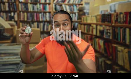 Man holds stopwatch and reaches hand forward in library building while smiling and showing stopwatch to camera; urgency time pressure. Stock Photo