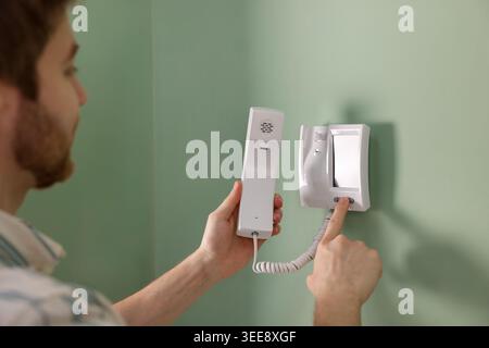 Man with handset pressing button on intercom panel indoors, closeup Stock Photo