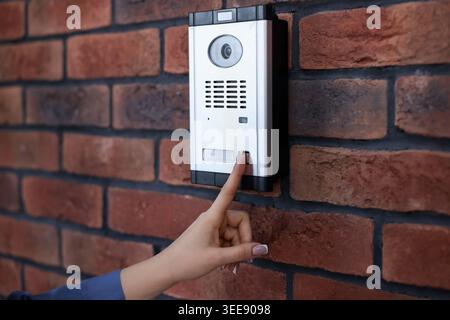 Woman pressing button on intercom panel near brick wall, closeup Stock Photo