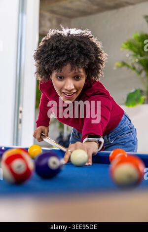 Leaning over blue-felt pool table in game-room African American woman in red-top lining up cue shot Stock Photo