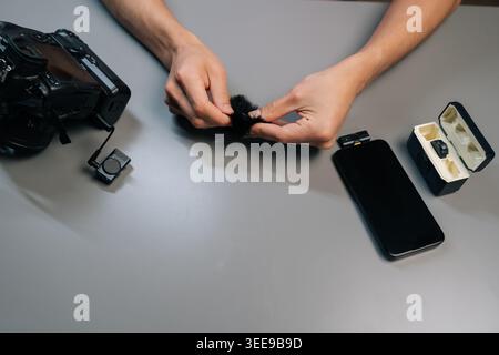 Top view of newsman attaching deadcat windshield to wireless lavalier microphone, preparing audio recording equipment for content creation and intervi Stock Photo