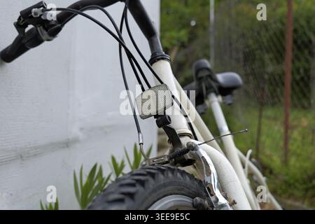 White bicycle leaning against a textured wall outdoors, showing handlebars, front wheel, reflector, and brake cables Stock Photo