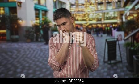 Man holding keys and hand on cheek for toothache in street shopping arcade wearing striped shirt; lost worry. Stock Photo
