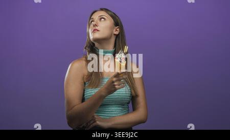 Woman holding ice cream cone, hand near mouth, looking up while wearing teal choker and striped top in studio; playful curiosity. Stock Photo