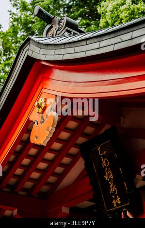 Ornate curved shrine roof with decorative wooden carvings and hanging plaque at Nezu Shrine, Bunkyō ward, Tokyo, Japan Stock Photo