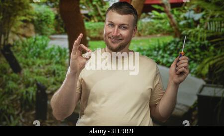 Man smiling holding screwdriver in right hand and making ok sign with left hand in forest; contentment diy repair. Stock Photo