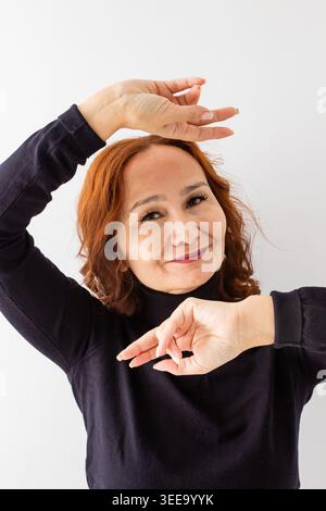 Mature redheaded woman making a frame with her hands around her face. Smiling lady looking at camera. Concept of creativity, beauty, self confidence a Stock Photo