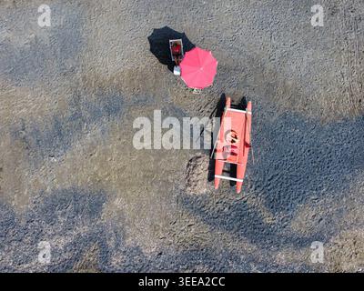 Aerial view of a lifeguard station on a sandy beach with a person under a red umbrella and a rescue boat in Imperia, Liguria, Italy. Stock Photo