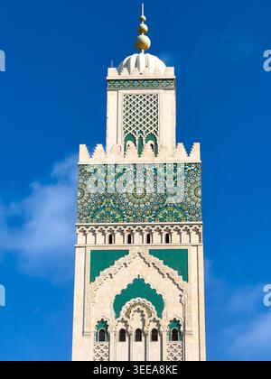 Hassan II Mosque minaret rises against a clear blue sky in Casablanca, showing ornate Moroccan tilework, arches, marble detail, and geometric decorati Stock Photo
