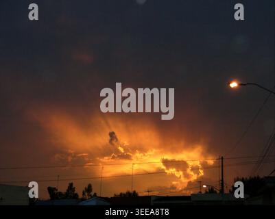 Golden sunset over city rooftops with light rays through clouds. Stock Photo