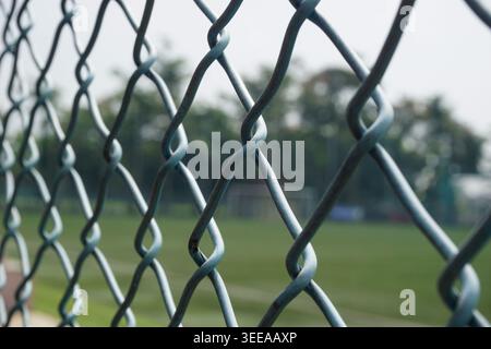 A green accordion wire fence with a blurred soccer field in the background. The composition gives the impression of a boundary or perspective Stock Photo