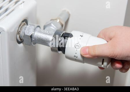 A man regulates the temperature on the radiator at home. Rising prices for heating in households. The concept of the energy crisis in Europe Stock Photo