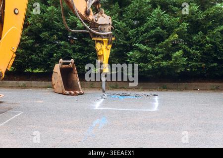 Heavy machinery uses pneumatic jackhammer on asphalt as workers prepare for construction in city setting. Stock Photo