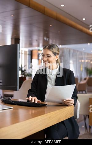 Female receptionist processing documents, using computer, working at front desk Stock Photo