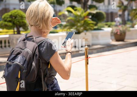 Female backpacker walking and using smartphone, capturing travel moments with smartphone at tourist destination, side profile Stock Photo