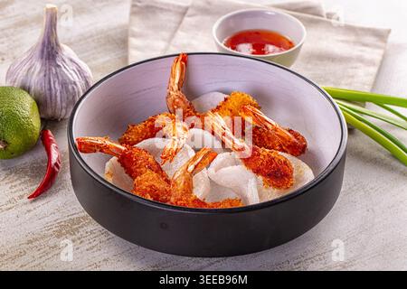 Appetizing bowl of golden deep-fried tempura prawns on rice crackers. Served with sweet chili sauce, lime, and garlic on a rustic white wood table. As Stock Photo