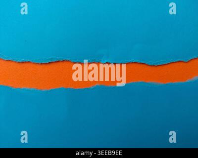 A horizontal strip of textured orange foam is revealed through a jagged tear in blue paper. Stock Photo