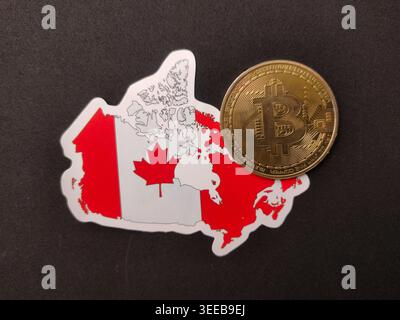 A single gold Bitcoin coin rests on the corner of a Canada map sticker against a black background. Stock Photo