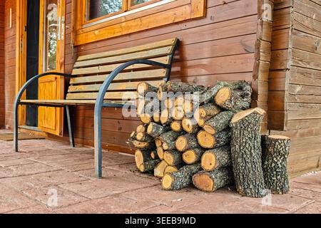 Logs of oak firewood stacked next to a wooden hut in the forest. Stock Photo