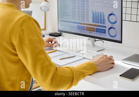Freelancer analyzing finance data at home office desktop with charts and graphs Stock Photo