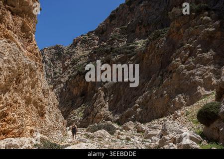 A woman hiking at the stunning Katholiko (or Avlaki) Gorge which features tall, steep, rugged and rocky cliffs, on a sunny day in Crete, Greece. Stock Photo