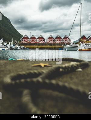 Starfish on coiled rope foreground with traditional red rorbu fishing cabins and sailboats at harbor in Lofoten northern Norway, photographed in summe Stock Photo