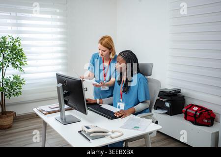 Two nurses collaborating on a computer, discussing patient records and health data Stock Photo