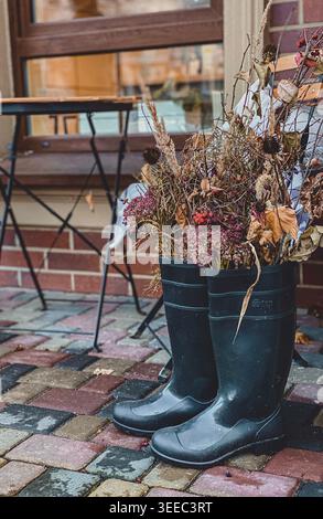 Rubber boots with dried flowers near cafe window, cozy autumn outdoor decor Stock Photo
