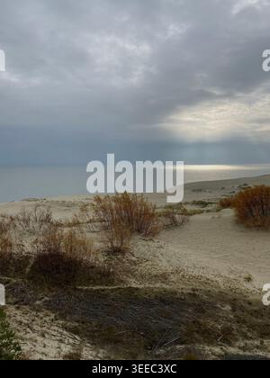 Moody coastal landscape with sand dunes, sea horizon and sun rays breaking through dramatic cloudy sky Stock Photo