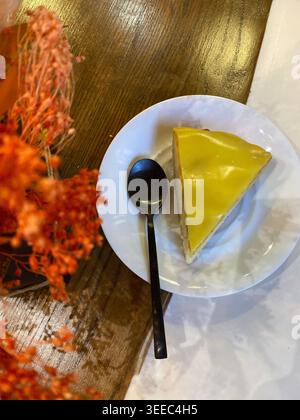 Slice of lemon cheesecake on white plate with spoon, cozy cafe table setting Stock Photo