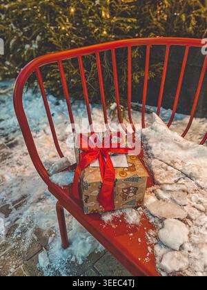 Wrapped Christmas gift on red bench outdoors, snowy festive winter atmosphere Stock Photo