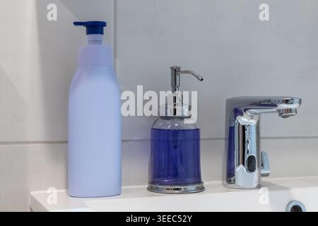 Bathroom sink accessories including a large pastel purple pump container and a clear glass soap dispenser with vibrant blue liquid are neatly arranged Stock Photo
