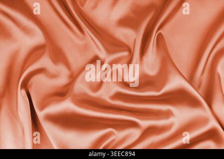 Crumpled, wrinkled orange colored glossy silk satin texture. Shiny smooth fabric with soft folds, cloth with wave drapery. Elegant and rich background Stock Photo
