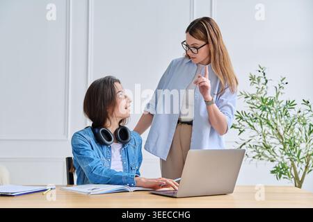 Female mentor pointing finger up and giving advice to young student using laptop in office Stock Photo