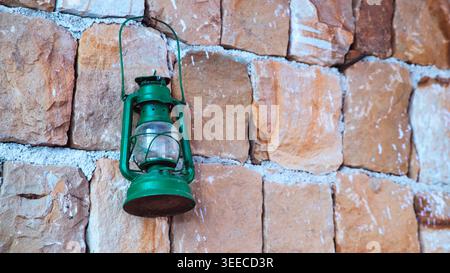 Old green lantern hanging on a rustic Moroccan stone wall, creating an authentic traditional atmosphere. Stock Photo