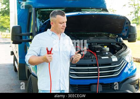 Man looking at a truck engine with battery cables in hands unsure how to fix the breakdown Stock Photo