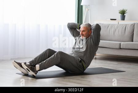 Athletic bearded senior man doing exercises for abs at home Stock Photo