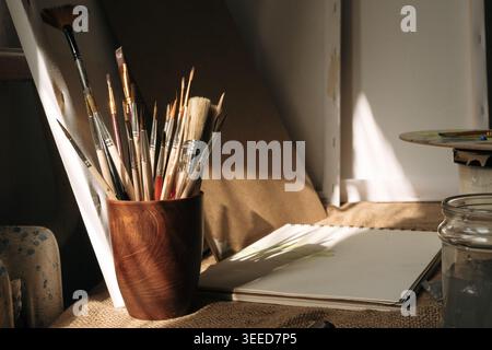 Close up of pottery cup with painting brushes and canvases in studio of artist. Creativity concept Stock Photo