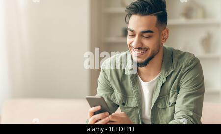 Young Man Smiles While Using Smartphone at Home in Casual Setting Stock Photo