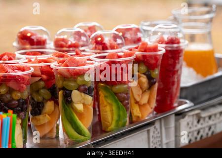 Variety of fresh cut tropical fruits in plastic cups for smoothie and juice at local street food market with selective focus and blurred background Stock Photo