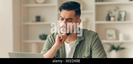 Young Man Thinking While Working on Laptop at Home in Casual Setting Stock Photo
