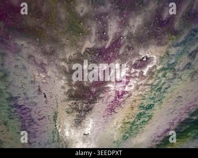 Abstract view of colorful soap suds and water flowing across a car windshield during an automated car wash with vibrant purple and green highlights Stock Photo