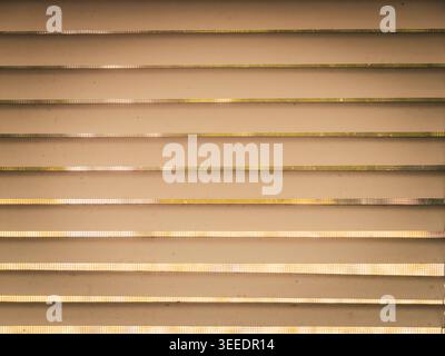 Warm toned abstract close up of horizontal textured slats with glowing light filtering through narrow gaps creating rhythmic geometric patterns Stock Photo