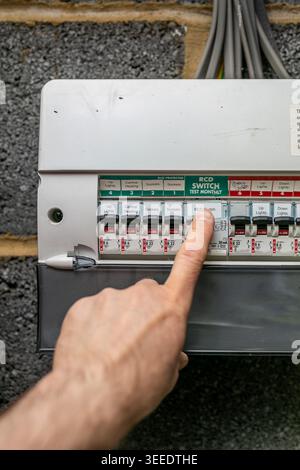 Person flicking a switch on a UK consumer unit, also known as a fuse box or distribution board, inside a residential property. Stock Photo
