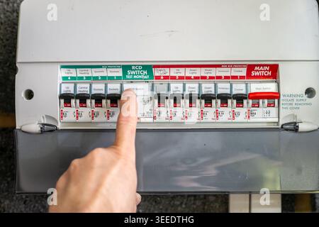 Person flicking a switch on a UK consumer unit, also known as a fuse box or distribution board, inside a residential property. Stock Photo