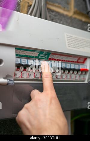 Person flicking a switch on a UK consumer unit, also known as a fuse box or distribution board, inside a residential property. Stock Photo