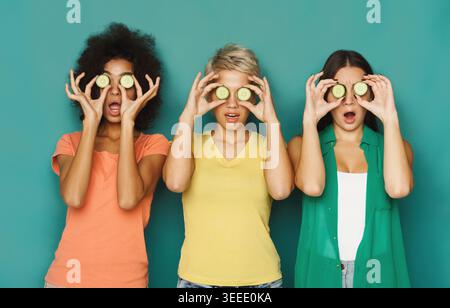 Three friends having fun with cucumbers in a colorful backdrop Stock Photo