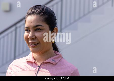 Woman in 30s standing outside by metal stair railing, wearing pink zip-up top and hoop earrings Stock Photo